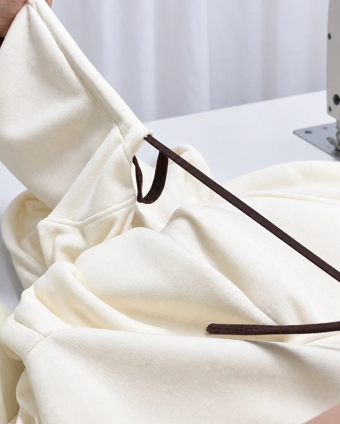 Brown drawcord passing through a stitched opening in a cream hood