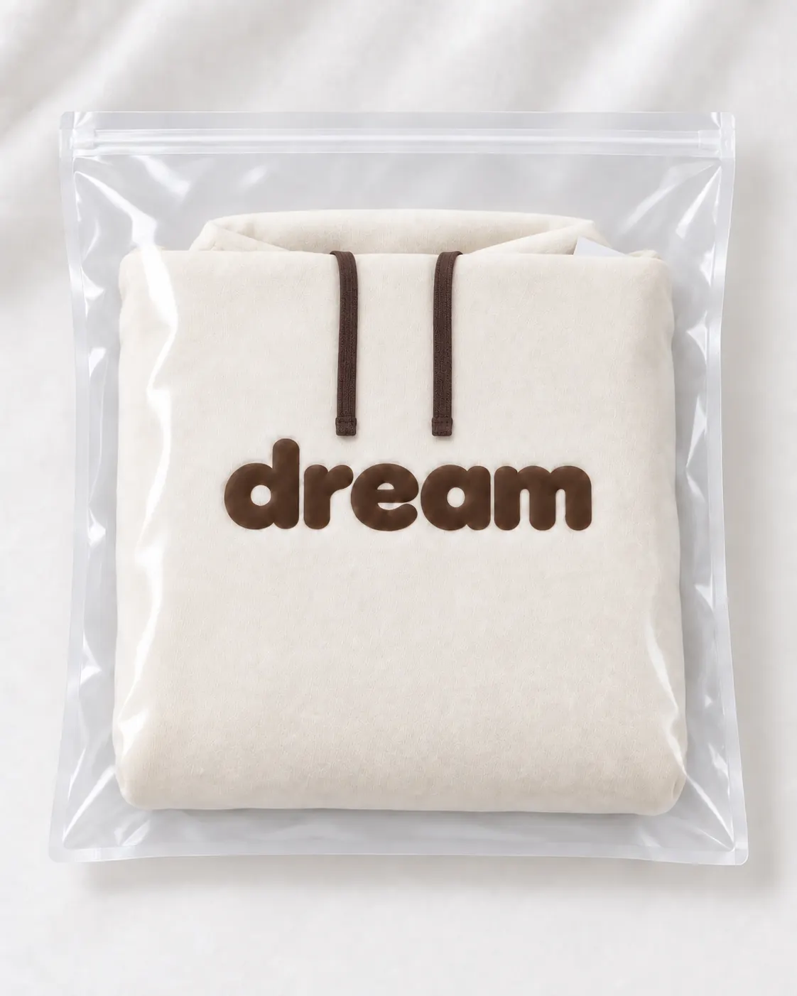 Folded cream hoodie with brown dream lettering inside a clear garment bag