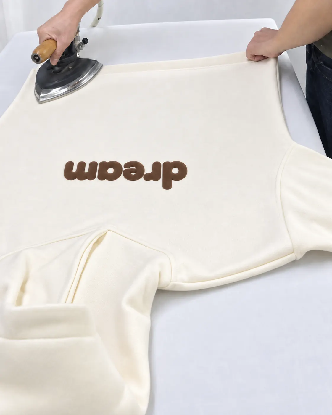 Cream hoodie with a brown dream print being pressed near the hem