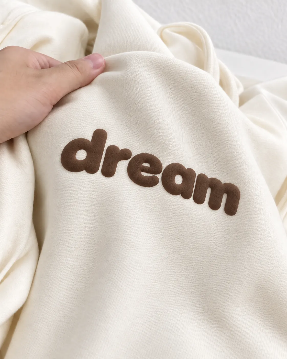 Raised brown dream lettering on cream hoodie fabric
