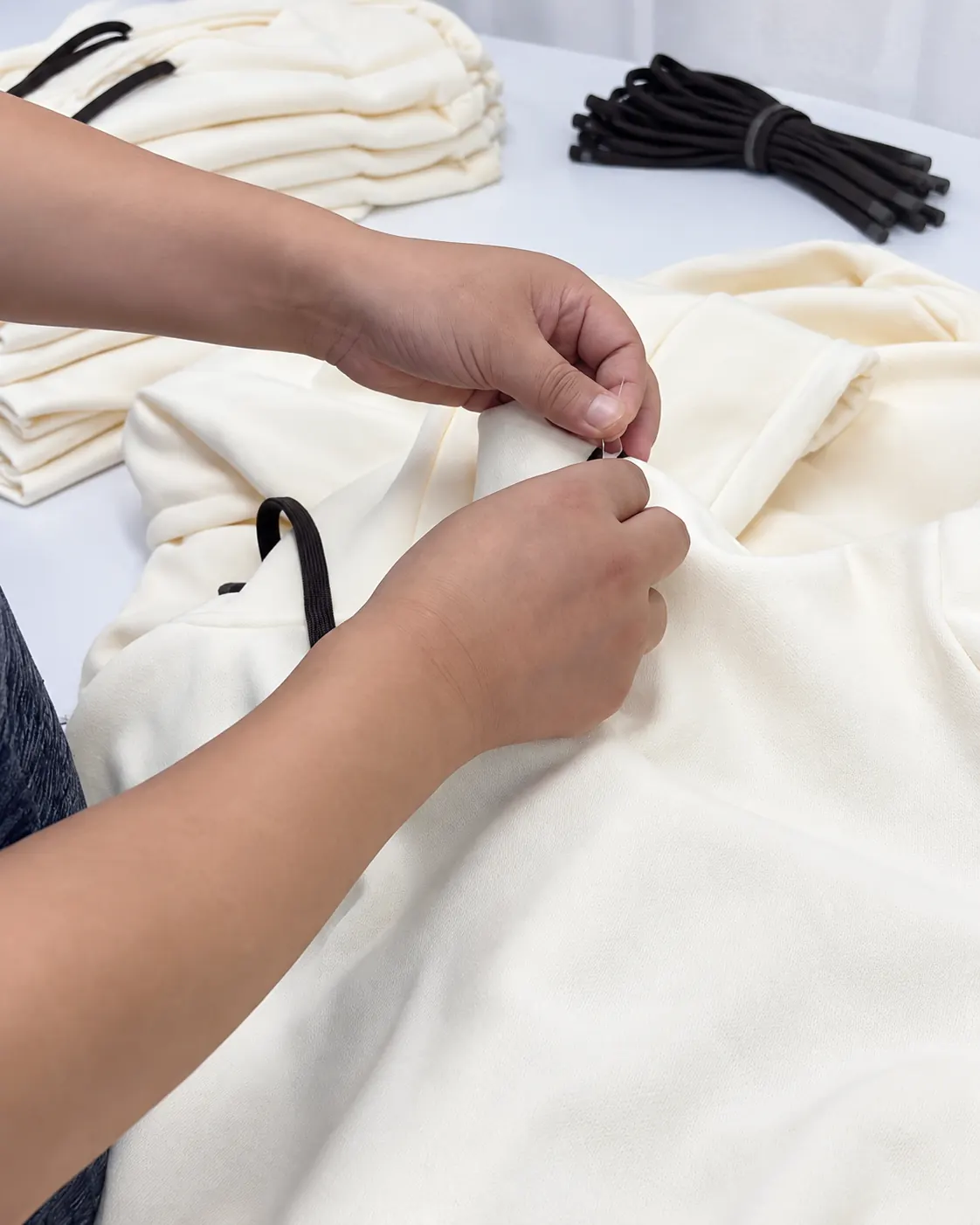 Hands working on loose threads on a cream hoodie